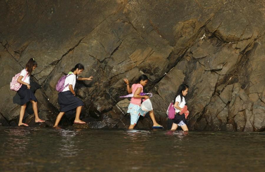 A woman accompanies some students as they wade in the shallow part of a rocky beach to their school to attend the first day of classes in Sitio Kinabuksan, Kawag village, Subic, Zambales Province, north of Manila. Long journey to school,journey to school