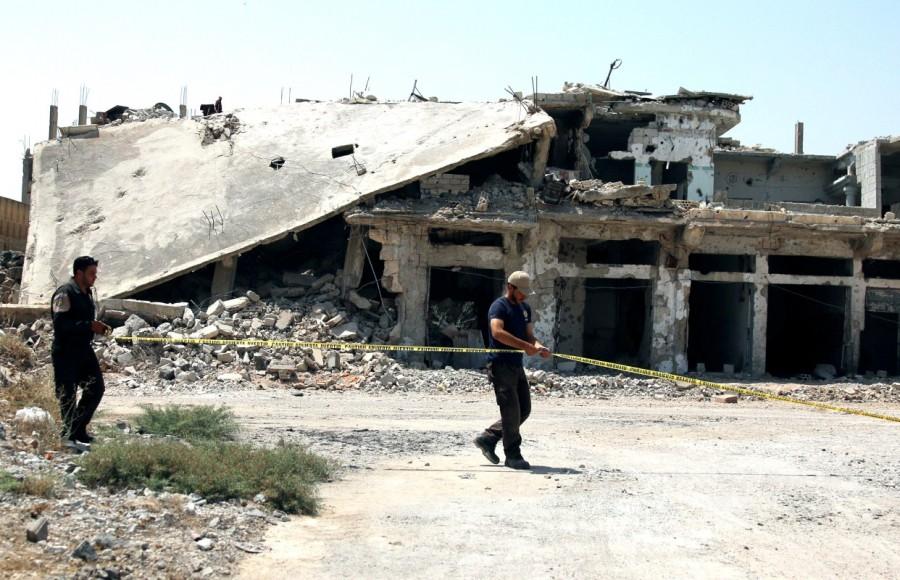 Civil defense members at a damaged site in Deraa. After the tape and signs are set up, rescue service members pile bags of dirt around the cluster bomb and place their own blue-and-white explosive cylinder inside, a red wire trailing from it. Syria,southwest Syria,cluster bombs,Syria cluster bombs