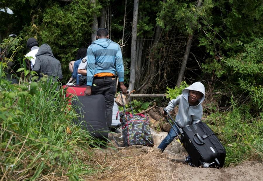 A family claiming to be from Haiti drag their luggage over the U.S.-Canada border into Canada from Champlain, New York, August 3, 2017. Hundreds of Haitians are streaming across the U.S. border into Canada, fearing deportation by U.S. President Donald Trump, according to aid workers and Quebec officials who have opened Montreal's Olympic Stadium to help process the influx. Canada from the U.S.,Canada-U.S. border,U.S. border,Quebec