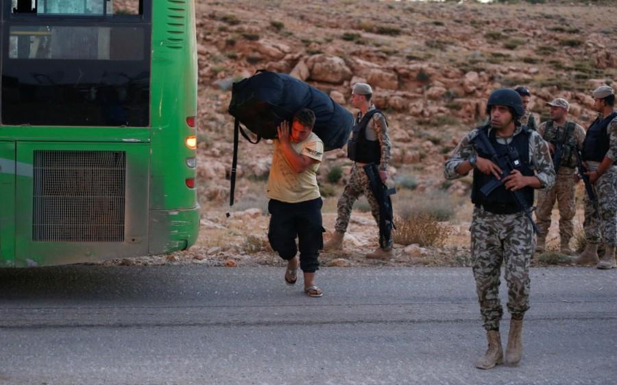 Lebanese policemen and Hezbollah fighters are seen as a Syrian man carries his bag near a bus in Jroud Arsal, Lebanon. Syrians evacuate Lebanon border,Lebanon border camps,Syrian militants,Syrian militants and refugees,Syrian refugees,Nusra Front militants