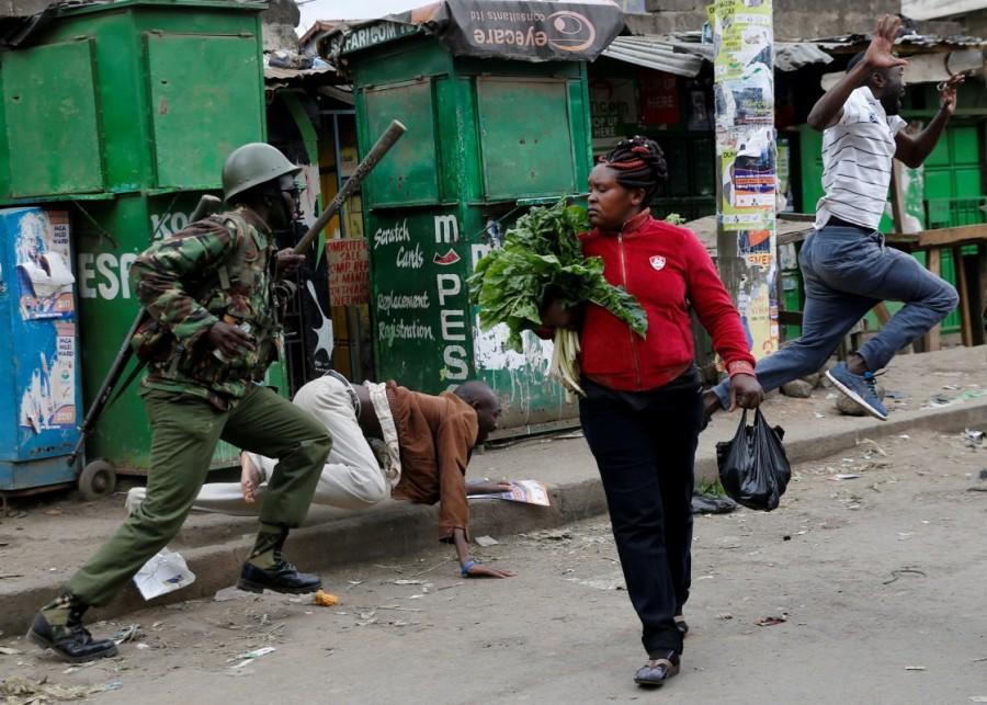 An anti riot policeman attempts to disperse people from the street as a woman carrying vegetables walks past in Mathare, in Nairobi, Kenya August 9, 2017. Raila Odinga,Kenya fake results,Kenya election,Kenya election fake results,Kenya's opposition leader Raila Odinga