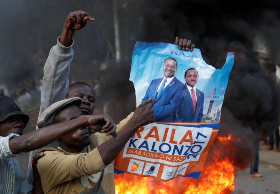A supporter of opposition leader Raila Odinga holds his poster in front of a burning barricade in Kibera slum in Nairobi, Kenya, August 9, 2017. Raila Odinga,Kenya fake results,Kenya election,Kenya election fake results,Kenya's opposition leader Raila Odinga