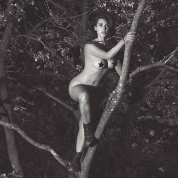 The black-and-white image that she has shared on social media shows Kim wearing only a pair of black boots as she climbs a tree, reports aceshowbiz.com. The reality TV star, 36, has placed her legs to prevent exposing her body parts. She has concealed her nipples in the photo with a pair of star emoticons. 