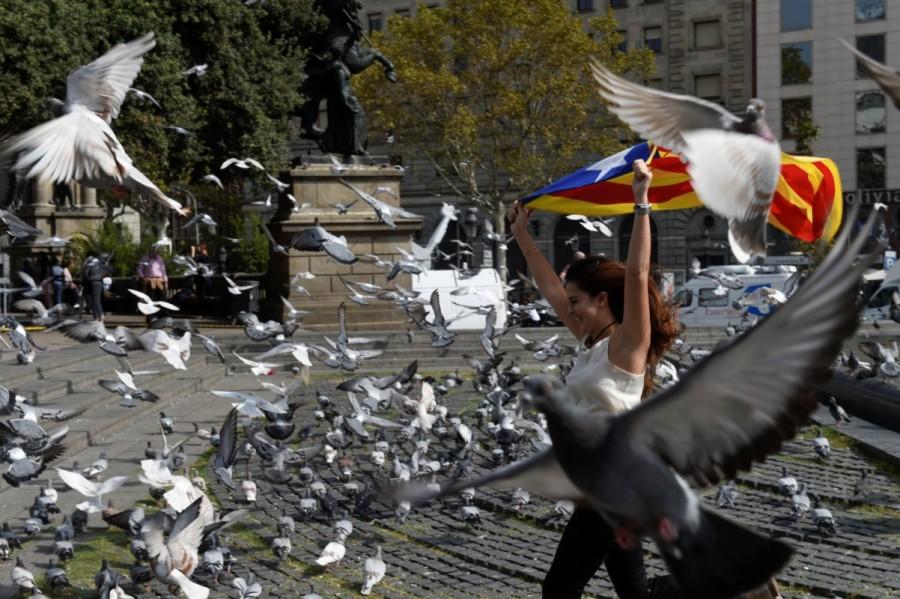 A woman runs through pigeons as she holds up an Estelada (Catalan separatist flag) during a protest a day after the banned independence referendum in Barcelona. Catalonia,Catalonia protests,Spanish police,violent secession vote