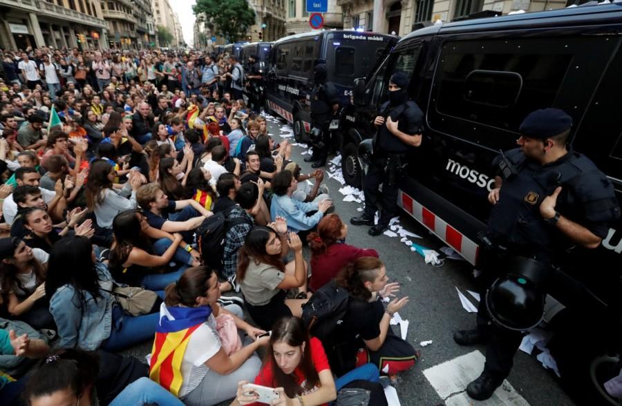 People sit during a protest as Catalan regional police officers stand guard outside National Police station, in Barcelona. Catalonia,Catalonia protests,Spanish police,violent secession vote