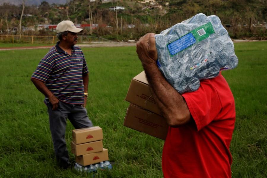 A man carries a case of water away from an HH-60 Blackhawk helicopter after soldiers working with 101st Airborne Division's "Dustoff" unit dropped off relief supplies during recovery efforts following Hurricane Maria, in Jayuya. Puerto Ricans,drinking water,search for water,Hurricane Maria hit,Hurricane Maria