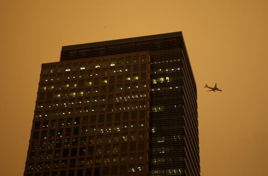 A plane flies past buildings in the Canary Wharf district as the sky turns red as dust from the Sahara carried by storm Ophelia filters sunlight over London. Ophelia turns London sky red,London sky red,London sky,Ophelia filters sunlight