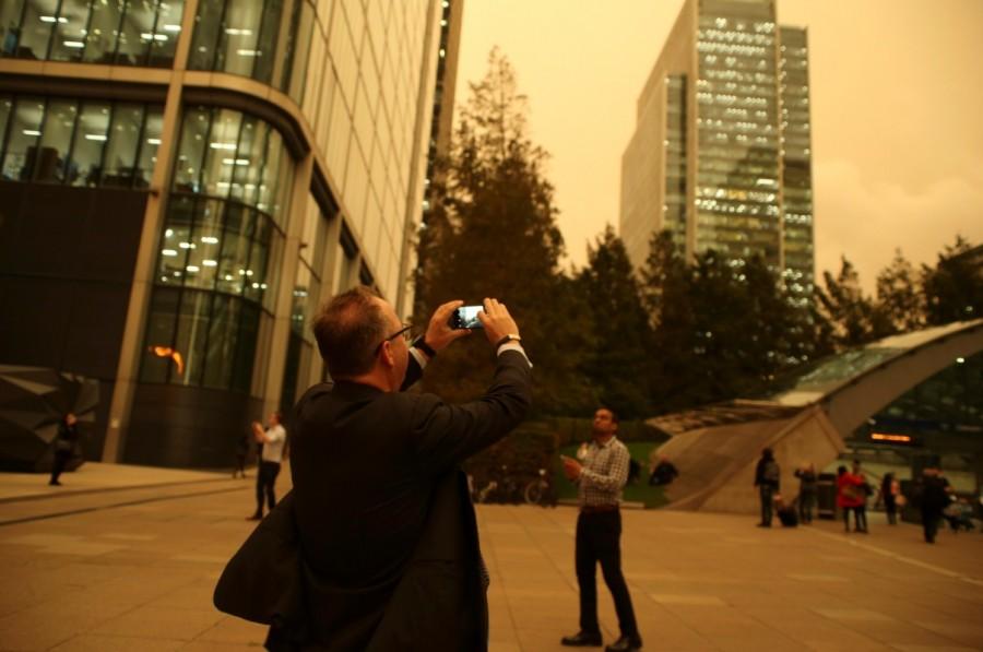 A man photographs the sky turning red over buildings in Canary Wharf as dust from the Sahara carried by storm Ophelia filters sunlight over London. Ophelia turns London sky red,London sky red,London sky,Ophelia filters sunlight