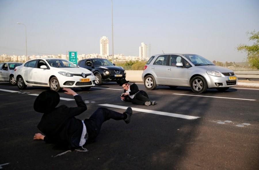 An ultra-Orthodox Jewish man reads from a prayer book as he lies on a road during a protest against the detention of members of their community who failed to report to a military recruiting office, near Modiin, Israel. Ultra-Orthodox protest,Ultra-Orthodox,Ultra-Orthodox protest against the detention,military recruiting office