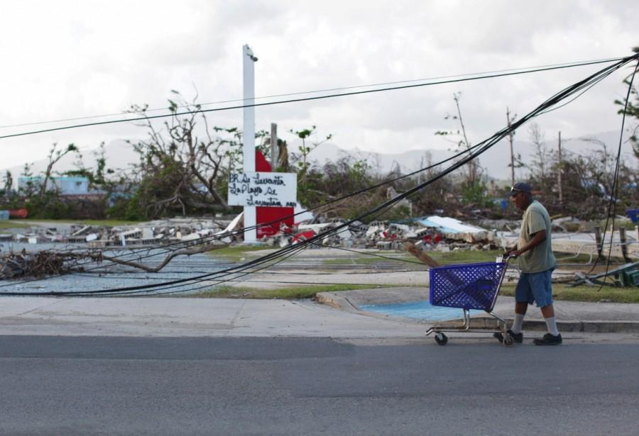 A man pushes a shopping cart past downed cables in Humacao. The writing in the back reads "Puerto Rico will rise." Puerto Rico,Hurricane Maria,Puerto Rico after Hurricane Maria