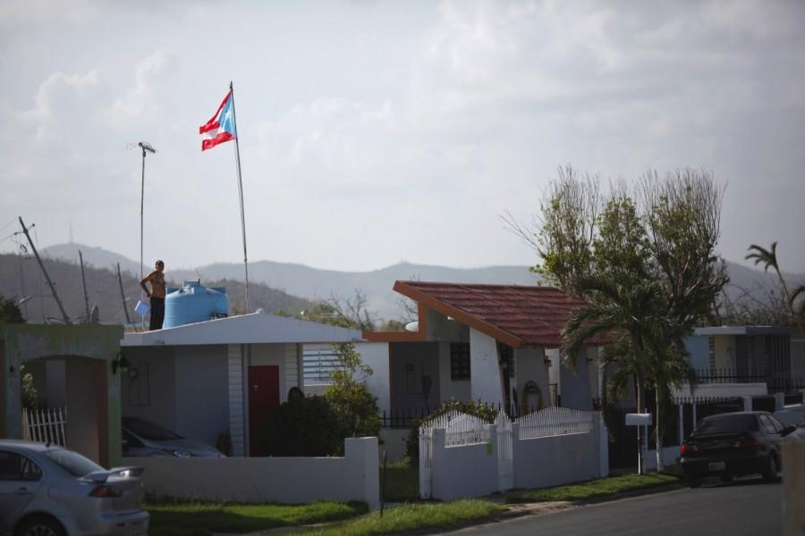 A man stands on the roof of his home and next to the Puerto Rican flag in Humacao. Puerto Rico,Hurricane Maria,Puerto Rico after Hurricane Maria