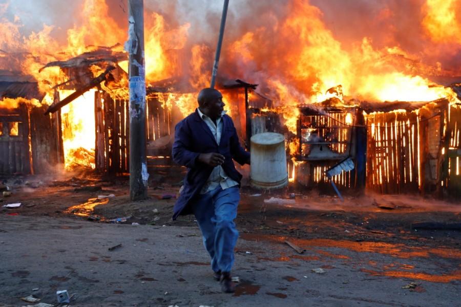 A man runs in front of a property that was set on fire by rioters in Kawangware slums in Nairobi. Kenya's election re-run,Clashes at Kenya,Kenya election rerun,Tensions high in Kenya