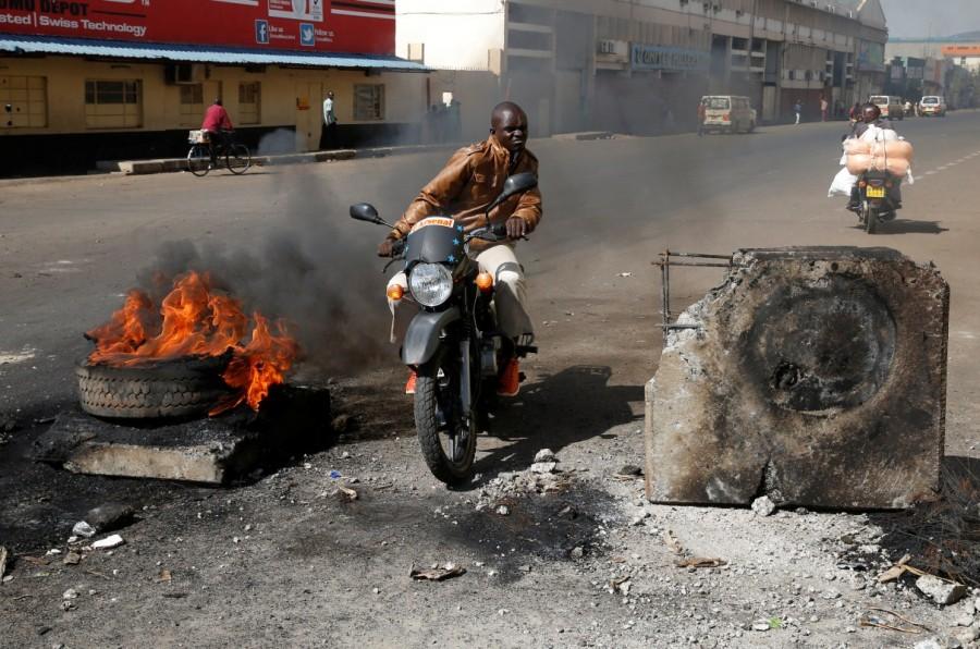 A motorcyclist rides past a burning barricade in Kisumu. Kenya's election re-run,Clashes at Kenya,Kenya election rerun,Tensions high in Kenya