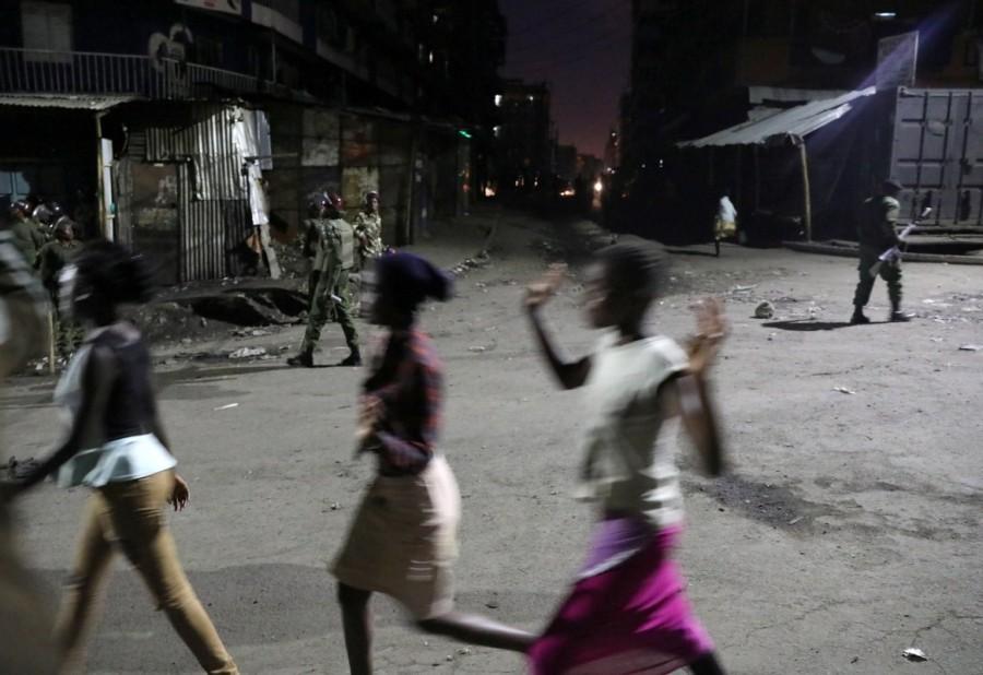 Women hurry past riot police in the slum area of Mathare in the capital Nairobi. Kenyan opposition,Kenyan leader,deadly violence,deadly violence in Kenya,Kenya deadly violence