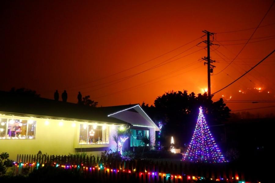 People stand on a roof of a home illuminated with Christmas lights to watch wildfire on a hillside burn during the Thomas Fire in Santa Barbara county near Carpinteria. Southern California wildfire,California wildfire,Los Angeles,wildfire,Thousands flee California wildfires