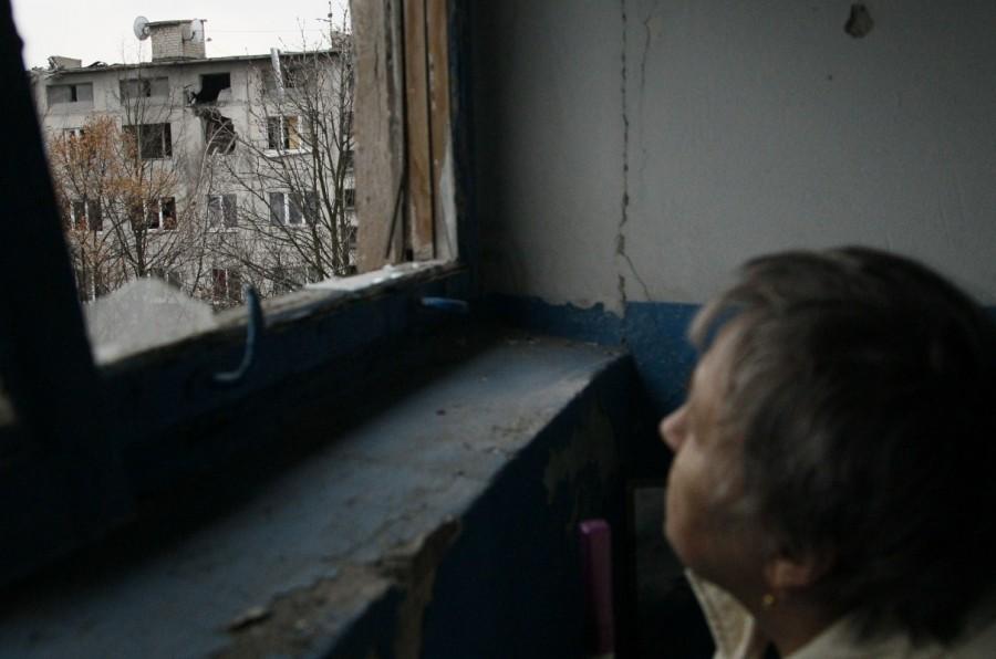 A woman watches a residential block damaged by recent shelling through a broken window in the rebel-held town of Yasynuvata, Ukraine December 21, 2017. Ukraine,Ukraine winter