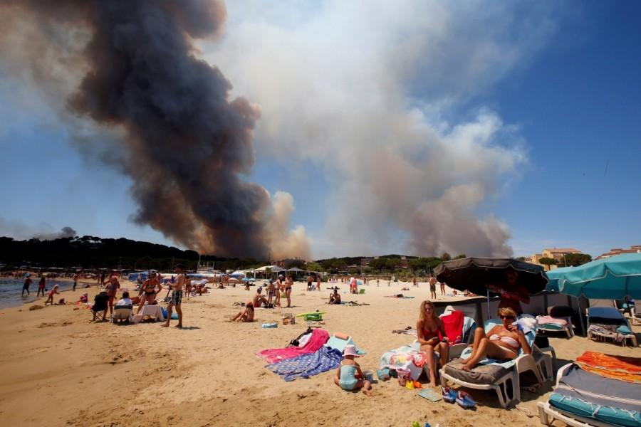 Smoke fills the sky above a burning hillside as tourists relax on the beach in Bormes-les-Mimosas, in the Var department, France, July 26, 2017. Natural disasters of 2017,disasters in 2017,2017 natural disasters,2017 disasters