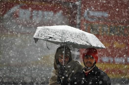 Men walk under an umbrella during snowfall on a cold winter morning in Srinagar.