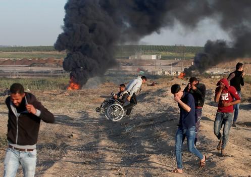 A wheelchair-bound Palestinian photographer is helped, as others react from tear gas, fired by Israeli troops, at a protest at the Israel-Gaza border where demonstrators demanded the right of Palestinians to return to their homeland, east of Gaza City April 1, 2018.