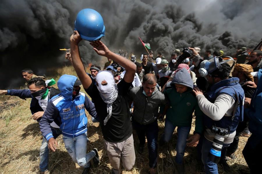 Palestinians evacuate a wounded journalist during clashes with Israeli troops at the Israel-Gaza border at a protest demanding the right to return to their homeland, in the southern Gaza Strip April 6, 2018. Gaza-Israel border,Israeli troops,Palestinian protesters,Gaza border