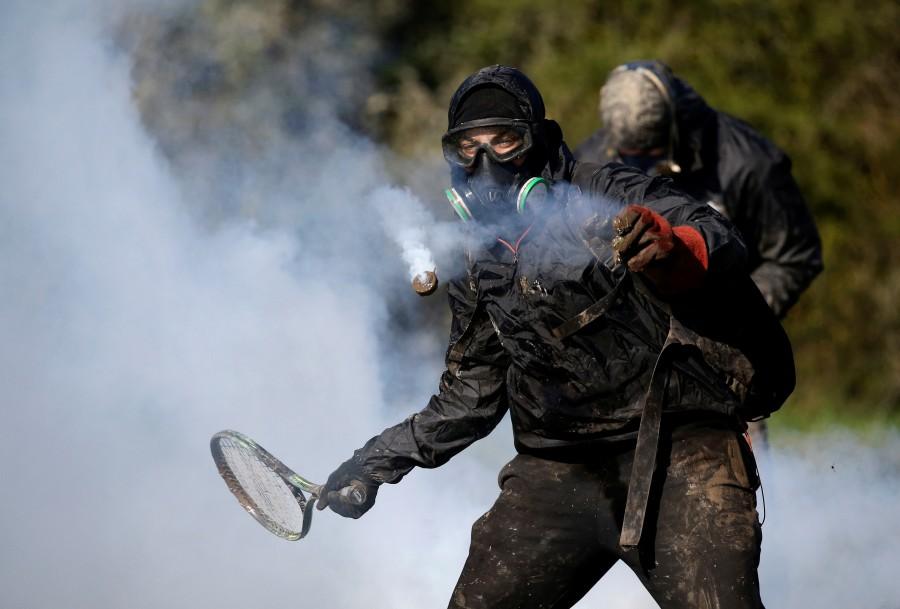 A protester uses a tennis racket to hit a tear gas canister during the evacuation operation by French gendarmes in the zoned ZAD (Deferred Development Zone) at Notre-Dame-des-Landes, near Nantes, France, April 11, 2018. French police,eco-activists,western France,French police swoop