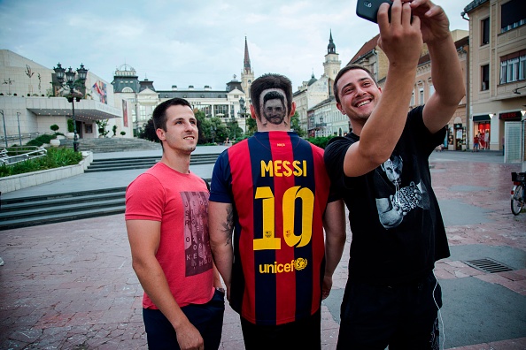 Two men take selfies with a football fan sporting a hair tattoo showing the portrait of Argentinian football player Lionel Messi in Novi Sad, Serbia, on June 10, 2018. - A Serbian hairdresser proposes to his clients to draw with scissors on the back of their heads portraits of football superstars Lionel Messi and Cristiano Ronaldo for the forthcoming World Cup in Russia. Mario Hvala gives his creativity free rain ever since, 18 years ago, he made with scissors a tarantula on a client's head after suggesting him: 'Let's do something different.' For the World Cup, which opens on June 14, 2018, he proposes to football afficionados to do the same thing with Messi and Ronaldo. FIFA World Cup fans,FIFA World Cup,Lionel Messi,Lionel Messi fans,Messi fans,Lionel Messi headshot,Messi headshot