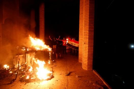 Iraqi protesters gesture near the burnt Iranian Consulate